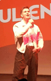 a man is singing into a microphone in front of an orange sign that says ulen