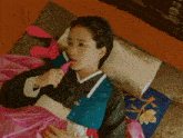 a woman in a traditional korean dress is laying on a bed with a pink blanket
