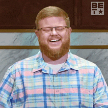 a man wearing glasses and a plaid shirt is smiling