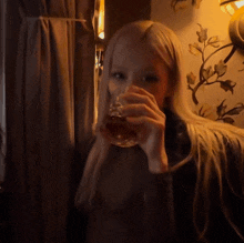 a woman with long blonde hair is drinking from a glass in a dark room