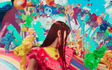 a woman in a pink dress is standing in front of a colorful background with balloons and candy .