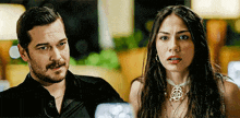 a man and a woman are sitting next to each other and the woman is wearing a necklace