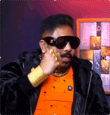 a man wearing sunglasses and an orange shirt has a gold chain around his neck