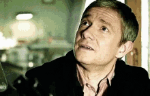 a man in a black jacket and pink shirt is looking up at something .
