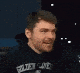 a man with a beard is wearing a black hoodie and laughing with his mouth open .