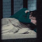 a man in a green shirt is laying on a bed with his head in his hands