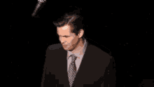 a man in a suit and tie is standing in the dark .