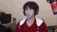 a young man wearing headphones and a red shirt is sitting in front of a microphone