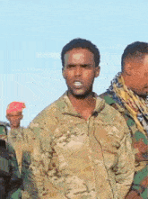 a man in a camouflage jacket is standing in front of a group of soldiers