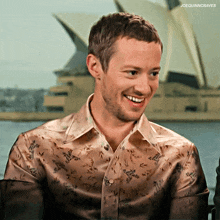 a man in a floral shirt is smiling in front of a building that says joequinncraves
