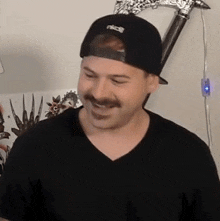 a man with a mustache is wearing a hat and a black shirt .