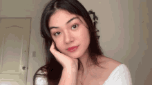 a woman in a white off the shoulder top has her hand on her chin