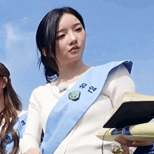 a woman wearing a blue sash with chinese writing on it is holding a book