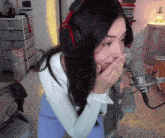 a woman wearing headphones stands in front of a microphone covering her mouth