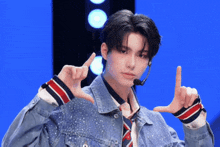 a young man wearing a microphone and a denim jacket makes a peace sign