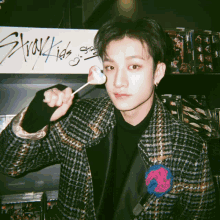 a man in a plaid jacket holds a lollipop in front of a sign that says stray kids