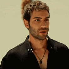 a man with a beard wears a black shirt and a necklace