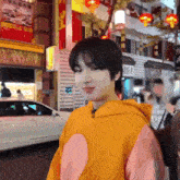 a young man wearing a yellow hoodie is standing on a city street .
