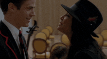 a man in a suit and tie talks to a woman wearing a black hat