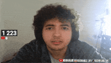 a man with curly hair is looking at the camera with the number 1223 behind him