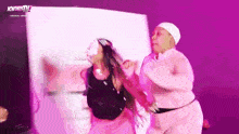two women are dancing on a stage in front of a pink wall .