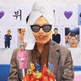 a woman wearing sunglasses and a towel wrapped around her head is holding a cake with candles that say bday