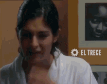 a woman in a white robe is standing in front of a picture of a man and the word el trece is on the bottom