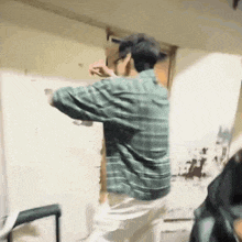 a man in a plaid shirt is standing in front of a white wall in a room .