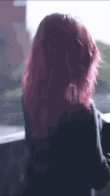 a woman with pink hair is wearing headphones and looking out a window