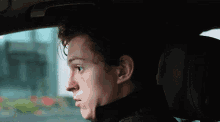 a young man is sitting in the driver 's seat of a car and looking out the window .