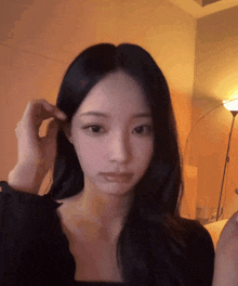 a woman with long black hair is touching her hair in front of a lamp