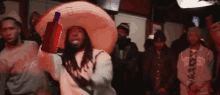 a man wearing a sombrero is holding a red bottle in front of a group of people .
