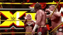 a group of wrestlers are standing in a wrestling ring with a woman standing next to them .
