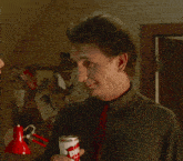 a man in a green shirt and red tie holds a can of diet coke