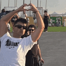 a man wearing sunglasses making a heart shape with his hands while wearing a white t-shirt that says iguana