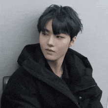 a young man wearing a black jacket is leaning against a wall and looking at the camera .