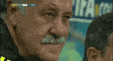 a man with a mustache is watching a soccer game with a score of 1-2