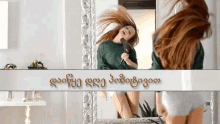 a woman blow drying her hair in front of a mirror with a banner in foreign language