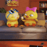 two cartoon chickens are sitting on a couch and one is wearing sunglasses and a pink bow