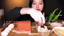 a woman wearing white gloves is cutting a piece of salmon