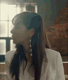 a woman wearing a white jacket and earrings is sitting in a room .