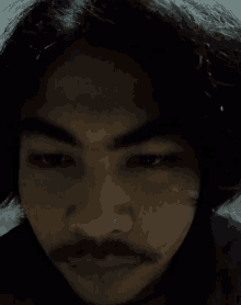 a man with a mustache looks at the camera with his eyes closed