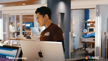 a man in a brown shirt is using an apple computer in a hospital