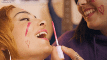 a woman is applying lip gloss to another woman 's face with the letters y and r on her face