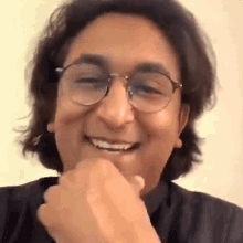 a man wearing glasses and a black shirt is smiling and covering his mouth with his hand .