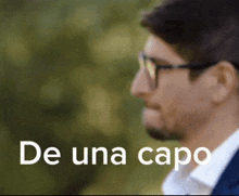 a close up of a man wearing glasses with the words de una capo behind him