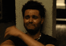 a man with a beard is crying while leaning against a concrete wall