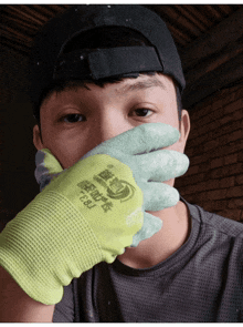 a man covering his face with a pair of green and yellow gloves that says ecru