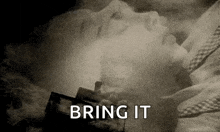 a black and white photo of a person laying on a bed with the words `` bring it '' written on the bottom .