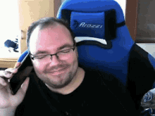 a man is sitting in a blue arozai chair talking on his phone